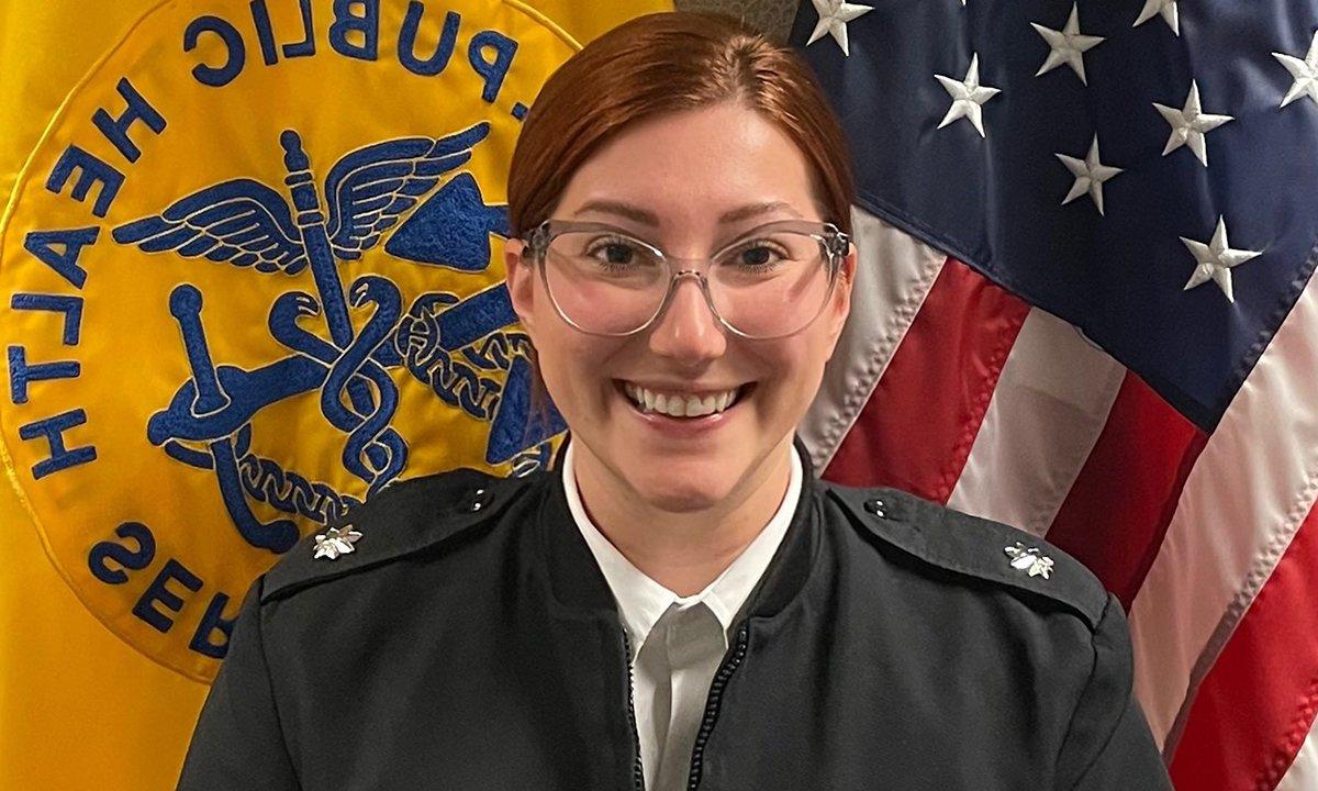 A woman in uniform in front of two flags.